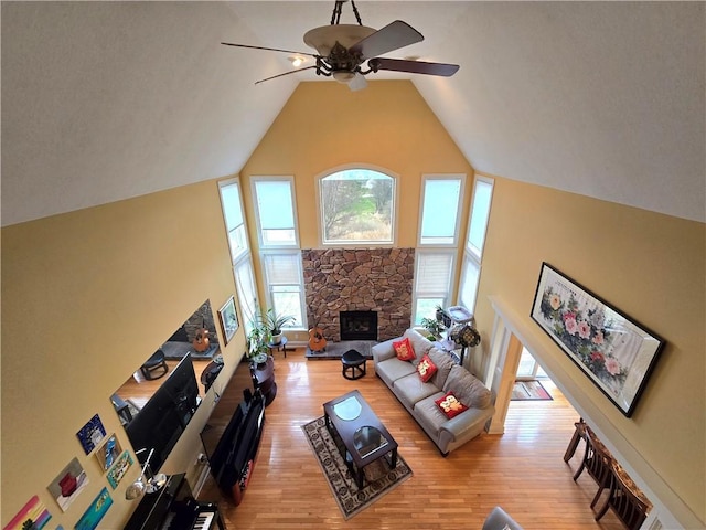 living area featuring ceiling fan, a stone fireplace, high vaulted ceiling, and light wood-style floors