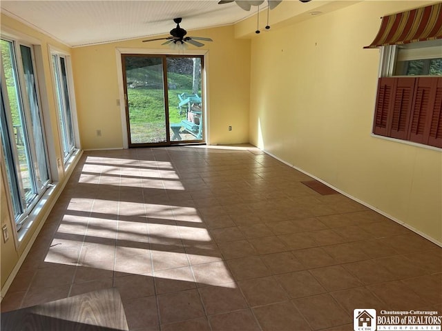 empty room featuring baseboards, a wealth of natural light, dark tile patterned flooring, and ceiling fan