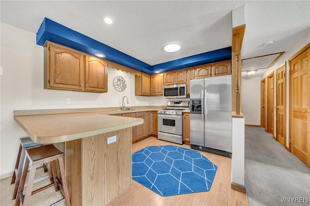 kitchen featuring light wood finished floors, a sink, a peninsula, a textured ceiling, and appliances with stainless steel finishes