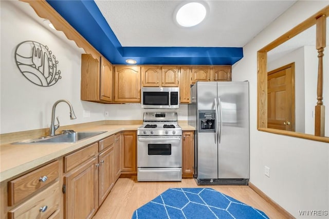 kitchen with light wood-style flooring, a sink, appliances with stainless steel finishes, and light countertops