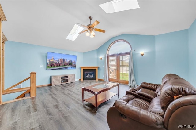 living room featuring vaulted ceiling with skylight, ceiling fan, visible vents, baseboards, and wood finished floors