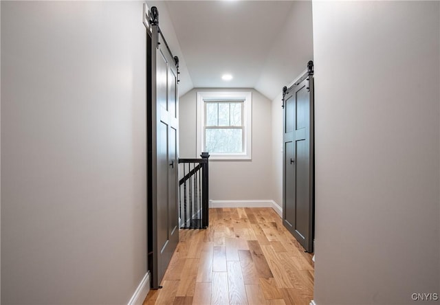 hallway with a barn door, an upstairs landing, light wood finished floors, baseboards, and lofted ceiling
