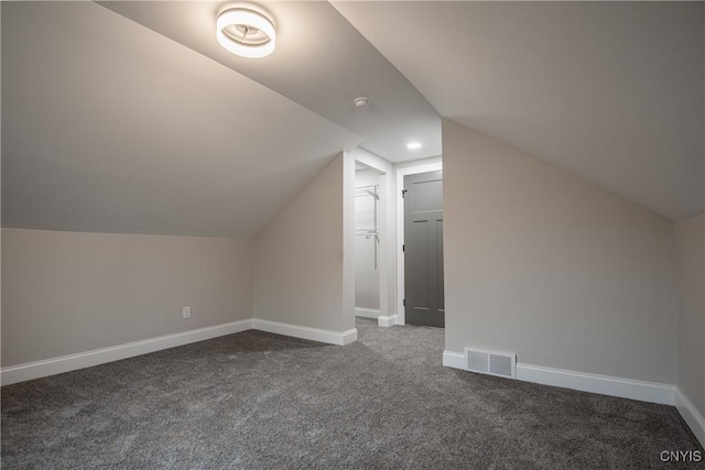 additional living space with lofted ceiling, visible vents, dark colored carpet, and baseboards
