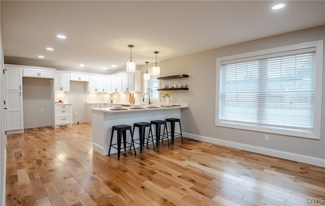 kitchen with white cabinetry, a kitchen bar, a peninsula, and light wood-style floors