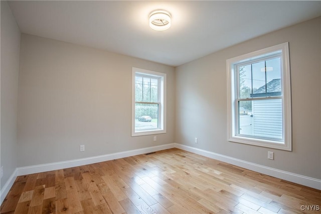 unfurnished room with light wood finished floors, visible vents, and baseboards