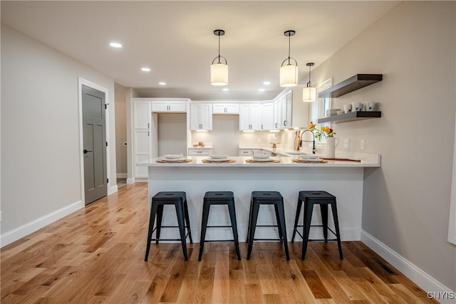kitchen with a kitchen bar, a sink, a peninsula, and white cabinetry