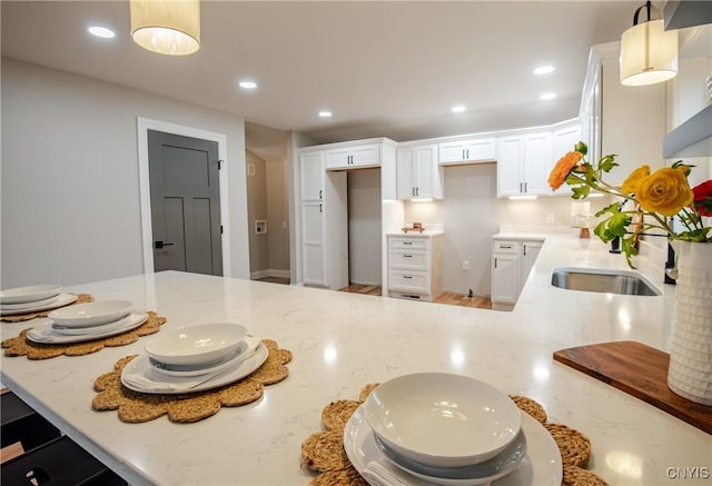 kitchen with light stone countertops, decorative light fixtures, a peninsula, and white cabinetry