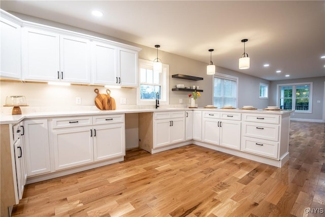 kitchen featuring hanging light fixtures, light wood-style floors, a sink, white cabinetry, and a peninsula