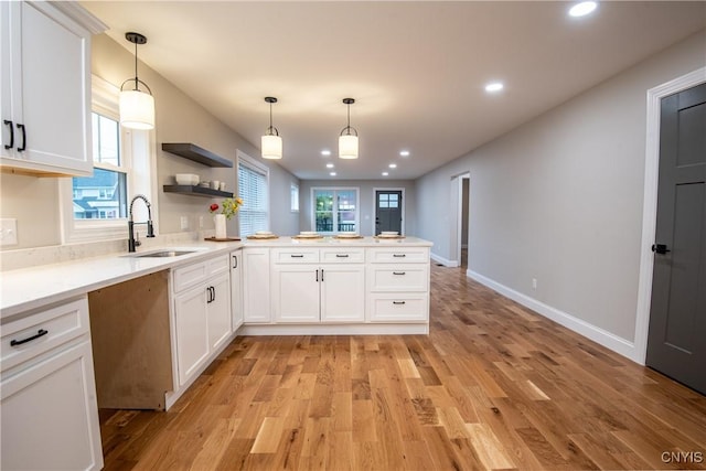 kitchen featuring light wood-style floors, a peninsula, white cabinetry, and a sink