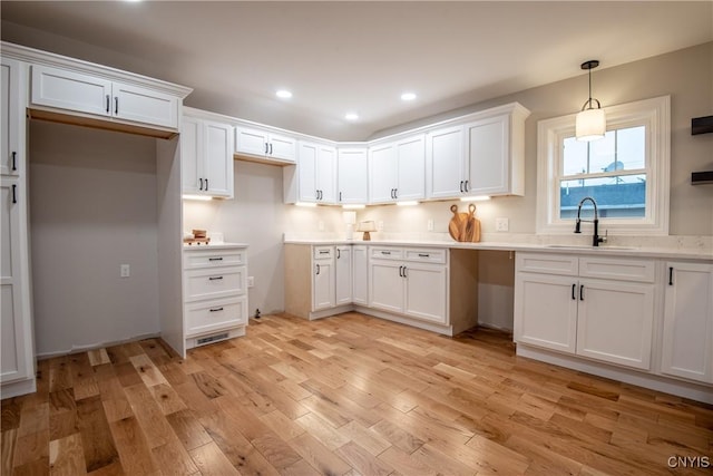 kitchen featuring white cabinets, decorative light fixtures, light wood finished floors, and a sink