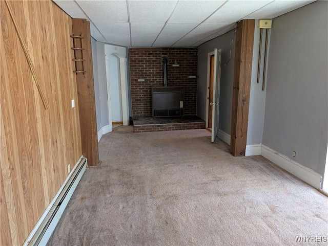 unfurnished living room featuring a wood stove, a paneled ceiling, carpet flooring, baseboards, and a baseboard radiator