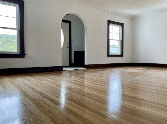 empty room with ornamental molding, arched walkways, wood-type flooring, and a textured wall