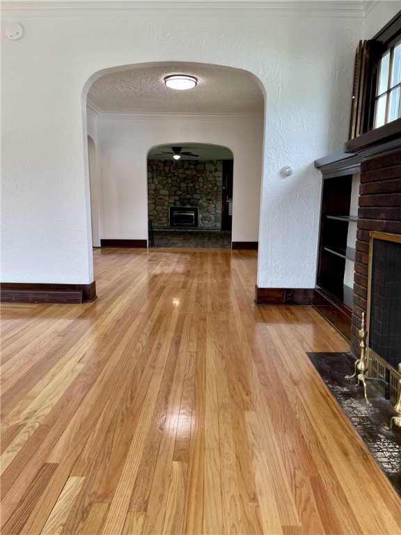 unfurnished living room featuring crown molding, ceiling fan, a fireplace with flush hearth, and wood finished floors