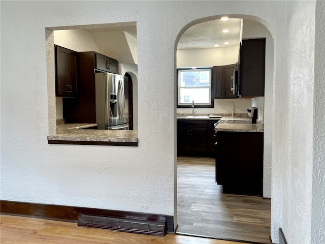 kitchen with arched walkways, a sink, a textured wall, and appliances with stainless steel finishes