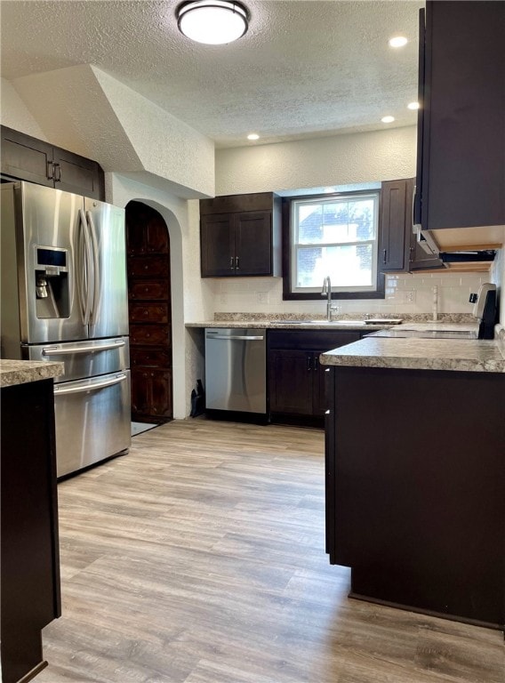 kitchen featuring stainless steel appliances, a textured ceiling, light wood-style flooring, and a sink