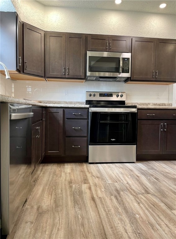 kitchen featuring appliances with stainless steel finishes, backsplash, light wood-style flooring, and dark brown cabinetry