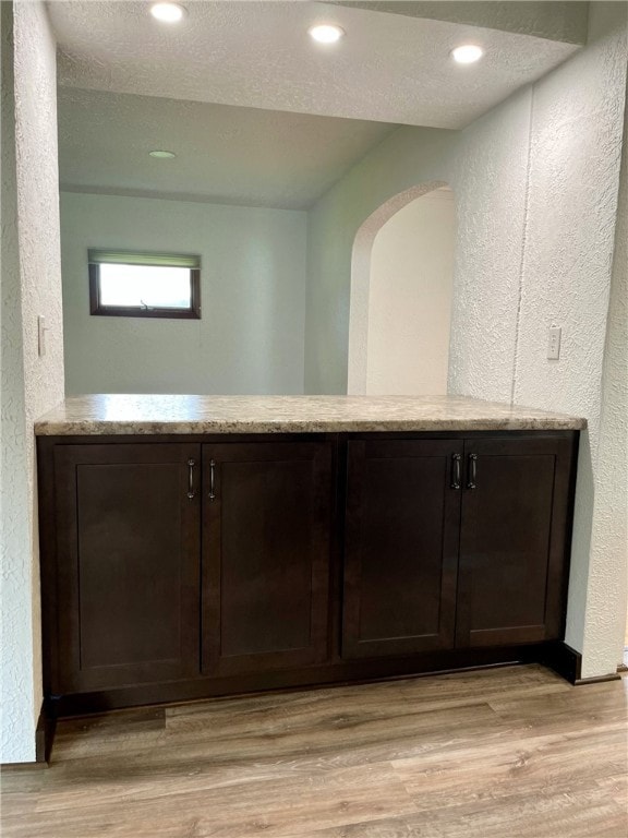 bar featuring a textured wall, recessed lighting, arched walkways, and light wood-style floors