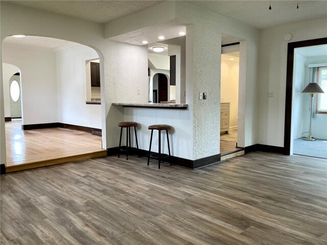 kitchen featuring a kitchen bar, a textured wall, wood finished floors, and baseboards