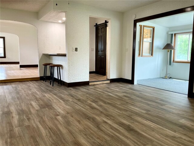 unfurnished room featuring wood finished floors, baseboards, a textured wall, and arched walkways
