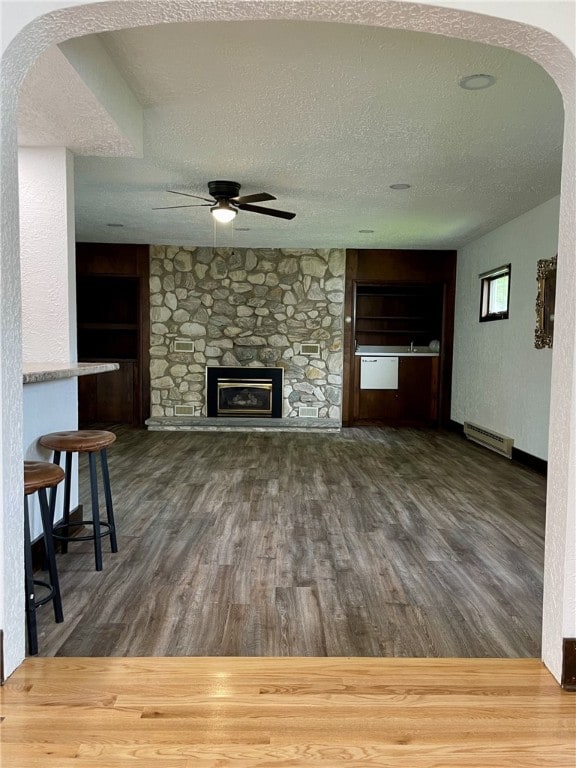 unfurnished living room with arched walkways, wood finished floors, a baseboard radiator, a ceiling fan, and a textured ceiling