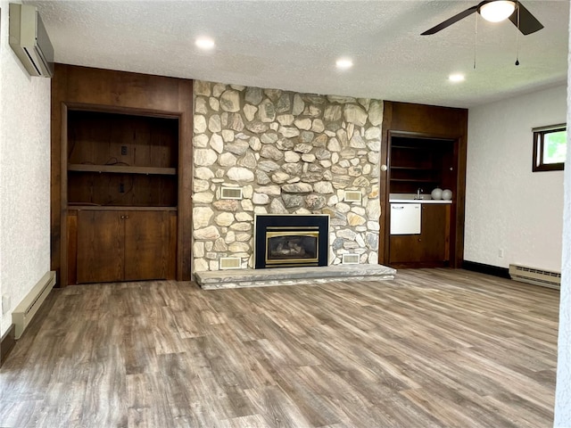 unfurnished living room with a baseboard heating unit, a wall unit AC, ceiling fan, a textured ceiling, and wood finished floors