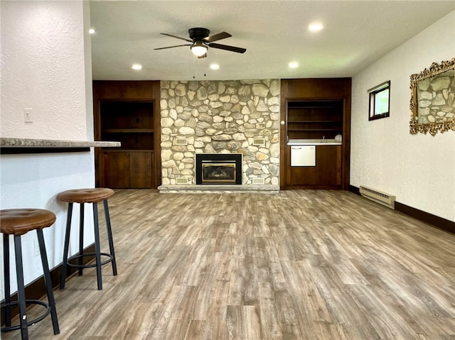 living area featuring built in shelves, ceiling fan, wood finished floors, and a baseboard radiator