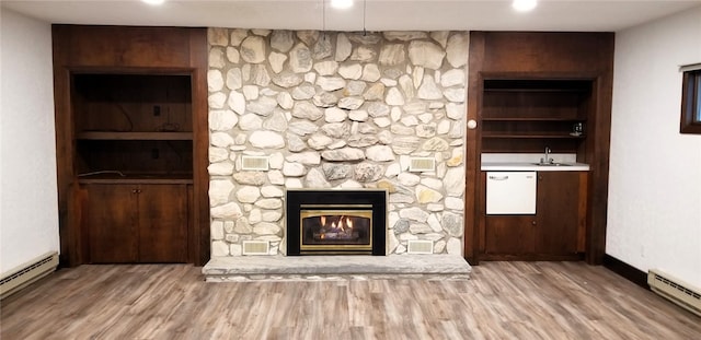 unfurnished living room featuring a sink, a baseboard radiator, a baseboard heating unit, wood finished floors, and a stone fireplace