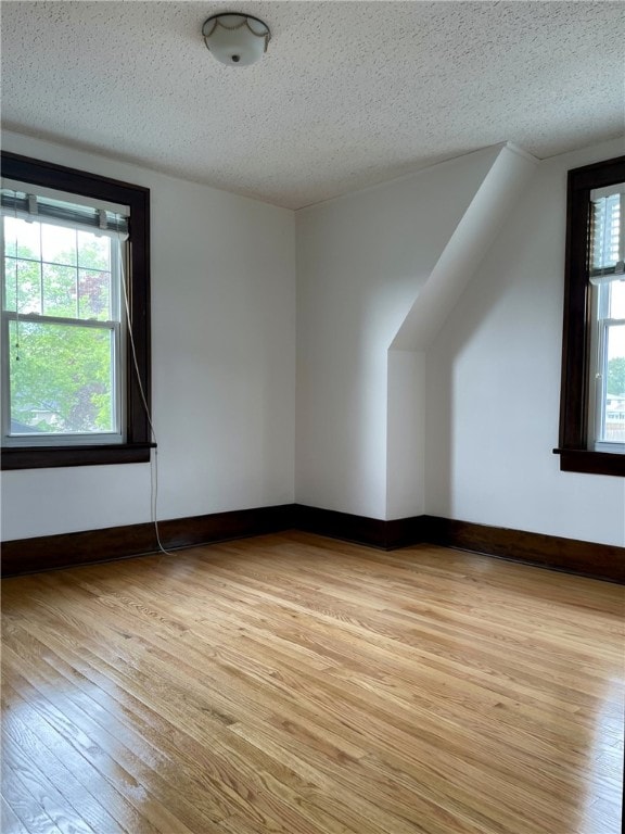 bonus room featuring a textured ceiling, light wood-type flooring, and baseboards