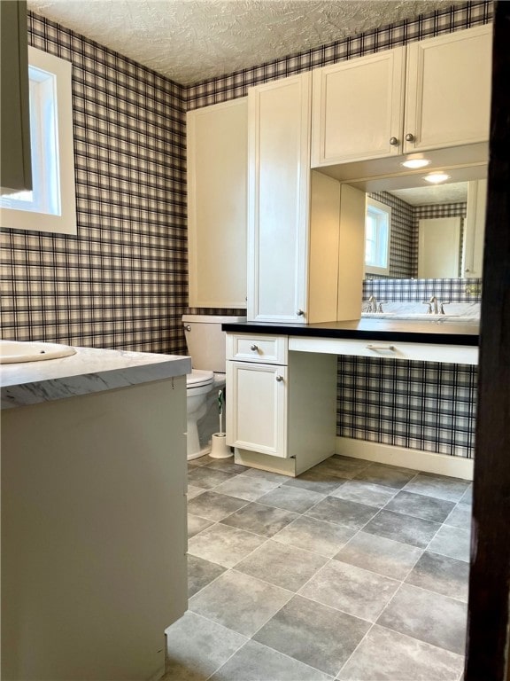 bathroom featuring wallpapered walls, toilet, a textured ceiling, and vanity