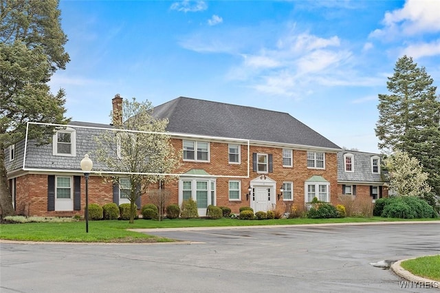 65 Guilford Ln Unit 5, Amherst, NY 14221 - view of front of property with uncovered parking, a front yard, brick siding, a chimney, and mansard roof