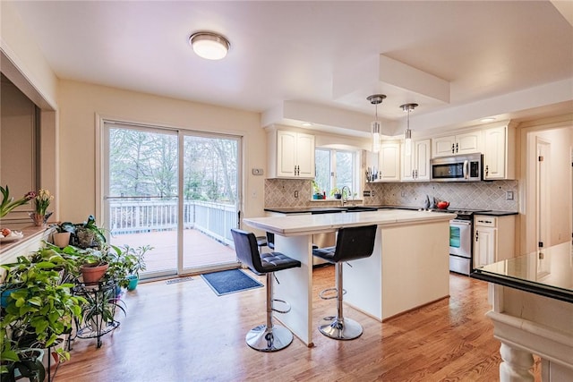 kitchen with backsplash, a kitchen bar, pendant lighting, appliances with stainless steel finishes, and light wood finished floors