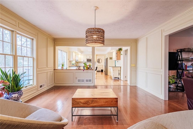 living room with a decorative wall, light wood finished floors, a textured ceiling, and visible vents