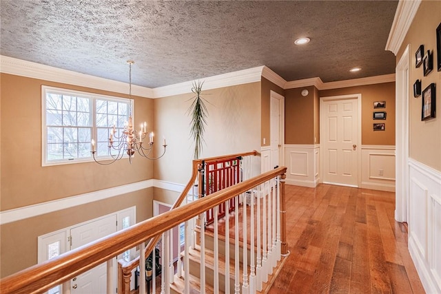 corridor featuring a notable chandelier, light wood finished floors, a wainscoted wall, an upstairs landing, and ornamental molding