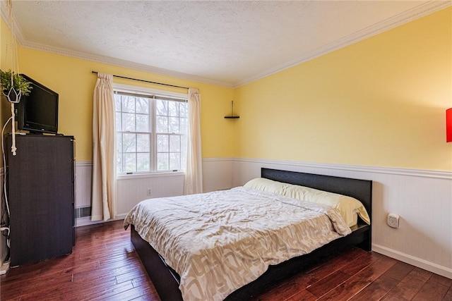 bedroom with wood-type flooring, a textured ceiling, wainscoting, and ornamental molding
