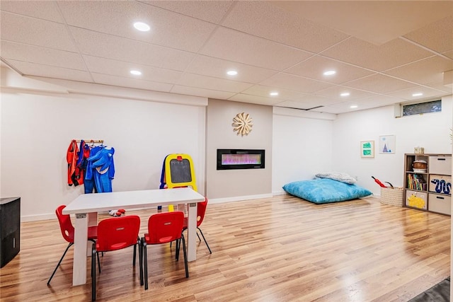 rec room with wood finished floors, baseboards, a glass covered fireplace, a drop ceiling, and recessed lighting