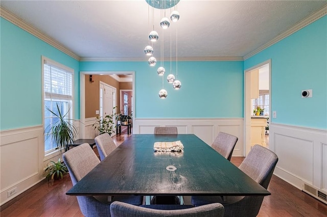 dining room featuring crown molding, visible vents, a decorative wall, wood finished floors, and a wainscoted wall