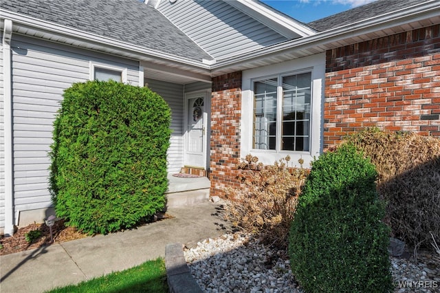 property entrance featuring a shingled roof and brick siding
