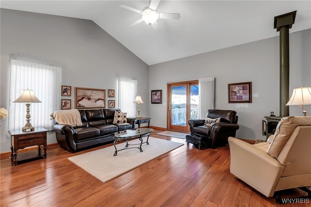 living area featuring a wood stove, a ceiling fan, high vaulted ceiling, and light wood-style floors