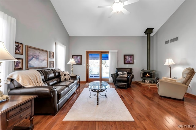 living area featuring a wood stove, visible vents, ceiling fan, vaulted ceiling, and wood finished floors