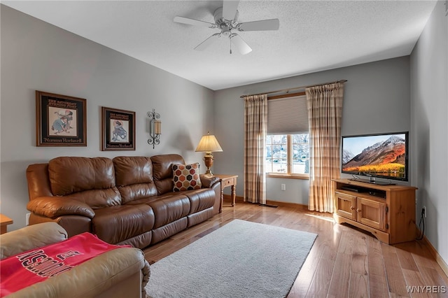 living area featuring baseboards, ceiling fan, a textured ceiling, and light wood finished floors