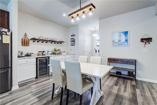 dining area featuring baseboards, beverage cooler, a bar, and light wood-style flooring