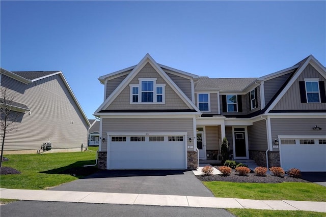 craftsman-style home featuring board and batten siding, aphalt driveway, a garage, stone siding, and a front lawn