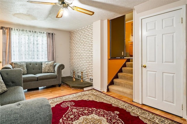 living room featuring a textured ceiling, ceiling fan, stairway, and wood finished floors