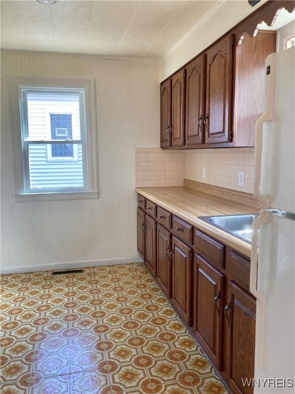 kitchen featuring light floors, freestanding refrigerator, light countertops, backsplash, and baseboards