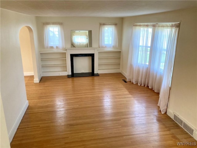 unfurnished living room featuring visible vents, arched walkways, wood finished floors, and a fireplace with raised hearth