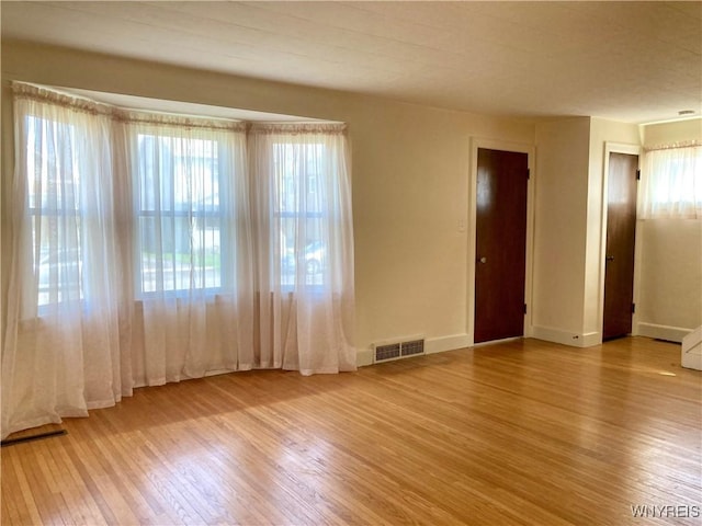 empty room featuring visible vents, wood finished floors, and baseboards
