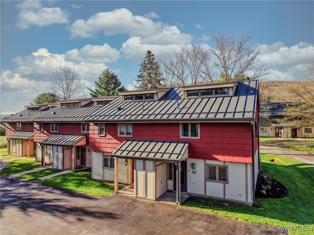 rear view of property with metal roof, a standing seam roof, a lawn, and stucco siding