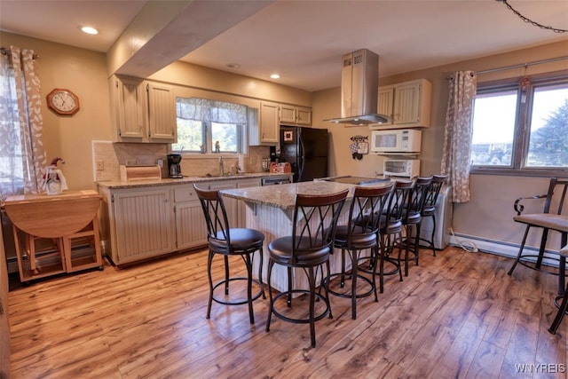 kitchen featuring island range hood, white microwave, light wood-style flooring, freestanding refrigerator, and a breakfast bar area