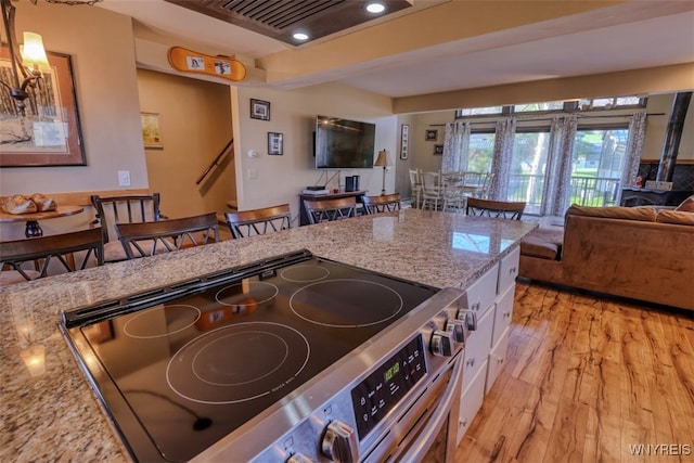kitchen with open floor plan, light stone counters, electric range, and light wood-style floors