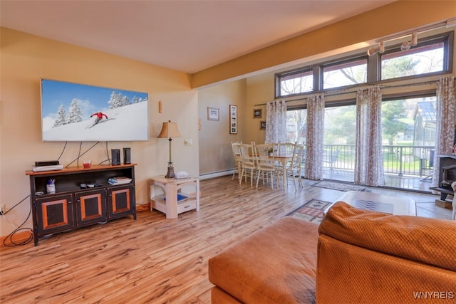 living room with baseboard heating, a wood stove, wood finished floors, and baseboards